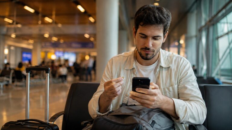 Viajero en un aeropuerto consulta el móvil y sostiene una tarjeta SIM antes de activar su conexión en Turquía