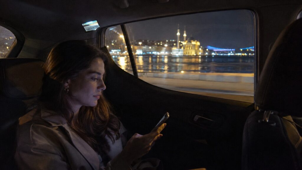 Pasajera viajando de noche en un taxi por Estambul con el Bósforo iluminado al fondo