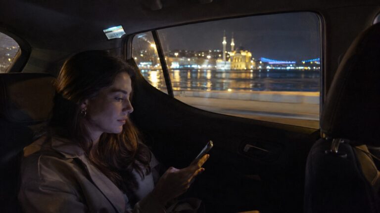 Pasajera viajando de noche en un taxi por Estambul con el Bósforo iluminado al fondo